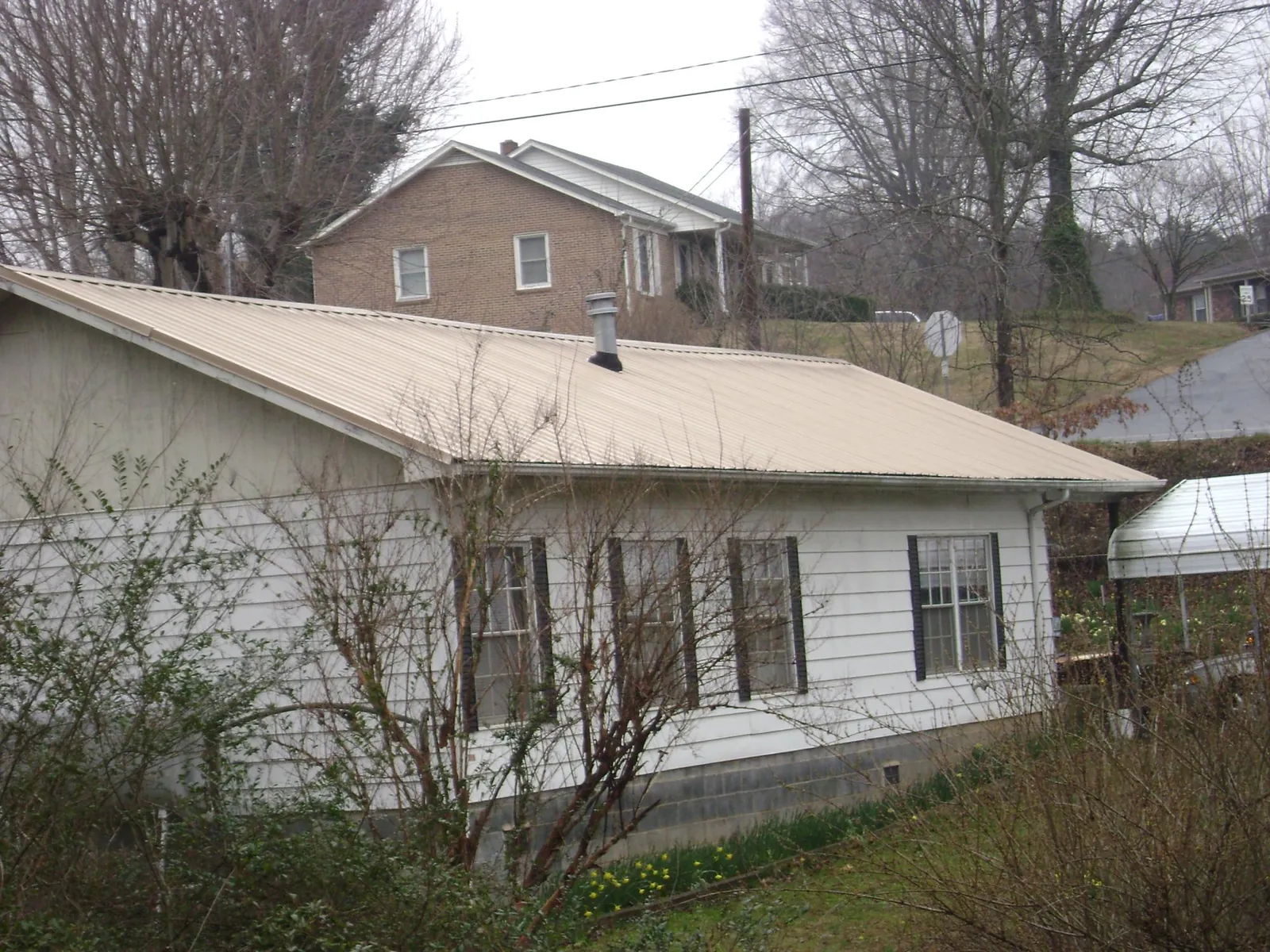 Tan metal roof on a white sided house set into a hillside — Commercial Roofing by Roofing Brothers in Millville